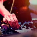 Hand adjusting controls on a DJ mixer with colorful lighting effects.