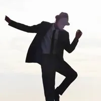 Silhouette of a person wearing a hat, suit, and tie in a dynamic dancing pose against a bright background.