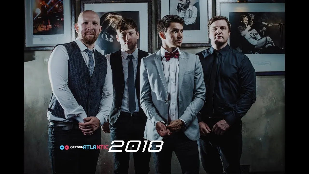 Four men dressed in formal attire standing in front of framed black-and-white photos, with text reading 'Captain Atlantic 2018'.